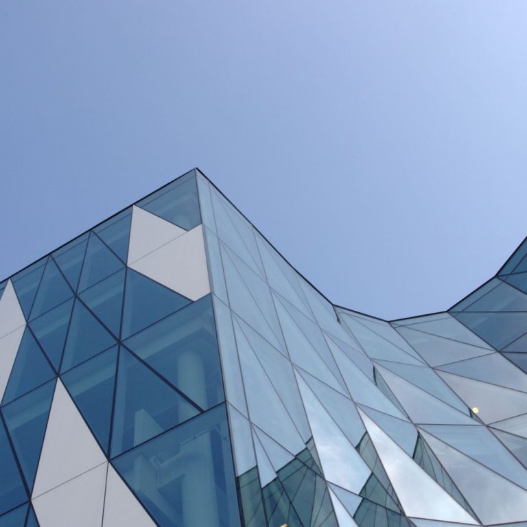 Image of a glass geometric building that is curved with sky in the background.