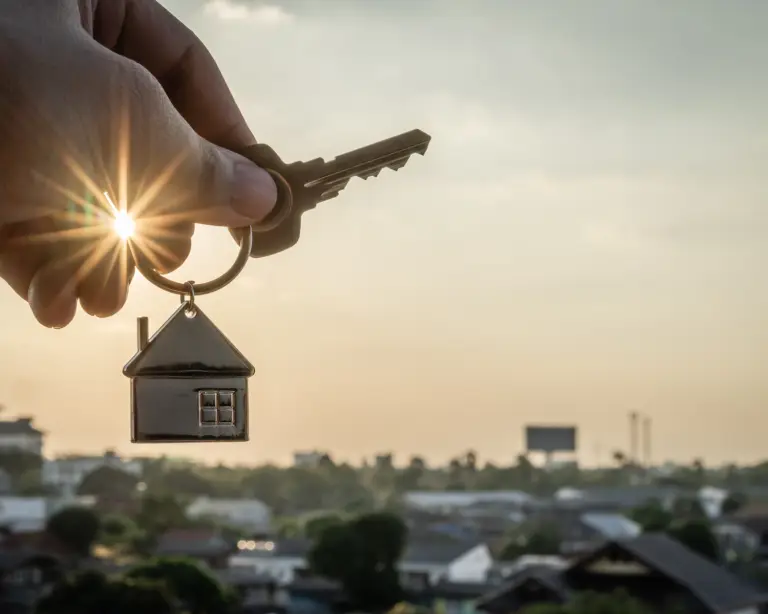 Image of a hand holding a house key with sun in background.