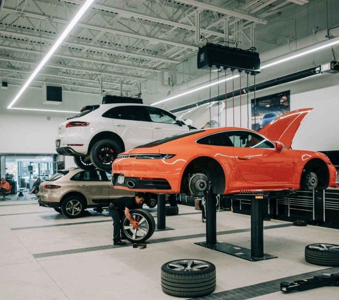 HOWELL-CONSTRUCTION-3 Image of a Porsche dealership interior with three vehicles up on lifts with a mechanic.