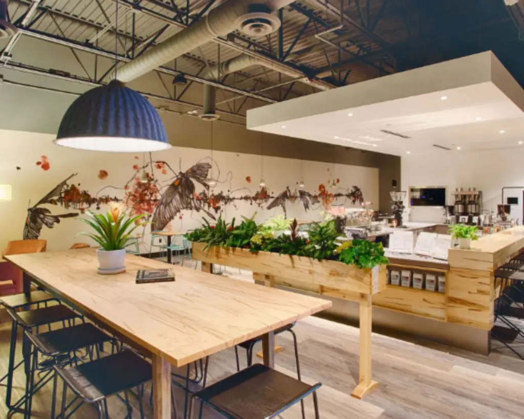 Image of an office building interior with work tables, shared area, and plants.