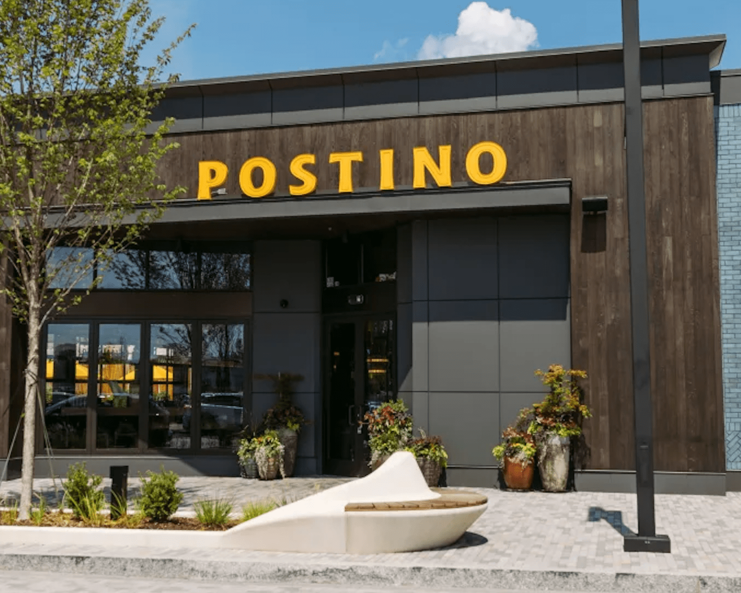 POSTINO-BALLANTYNE-1 Image of a modern wood restaurant exterior with large yellow Postino sign and glass windows.