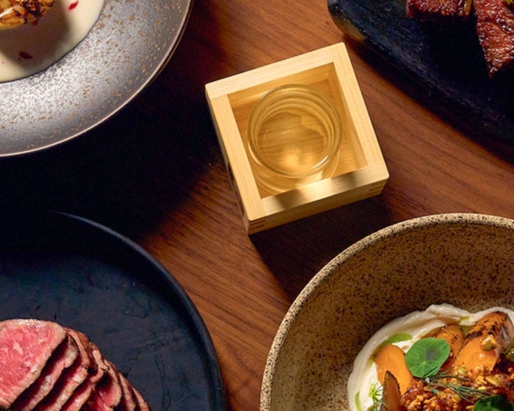 Uchiko Denver food presentation with a glass of sake inside of a small wooden box.