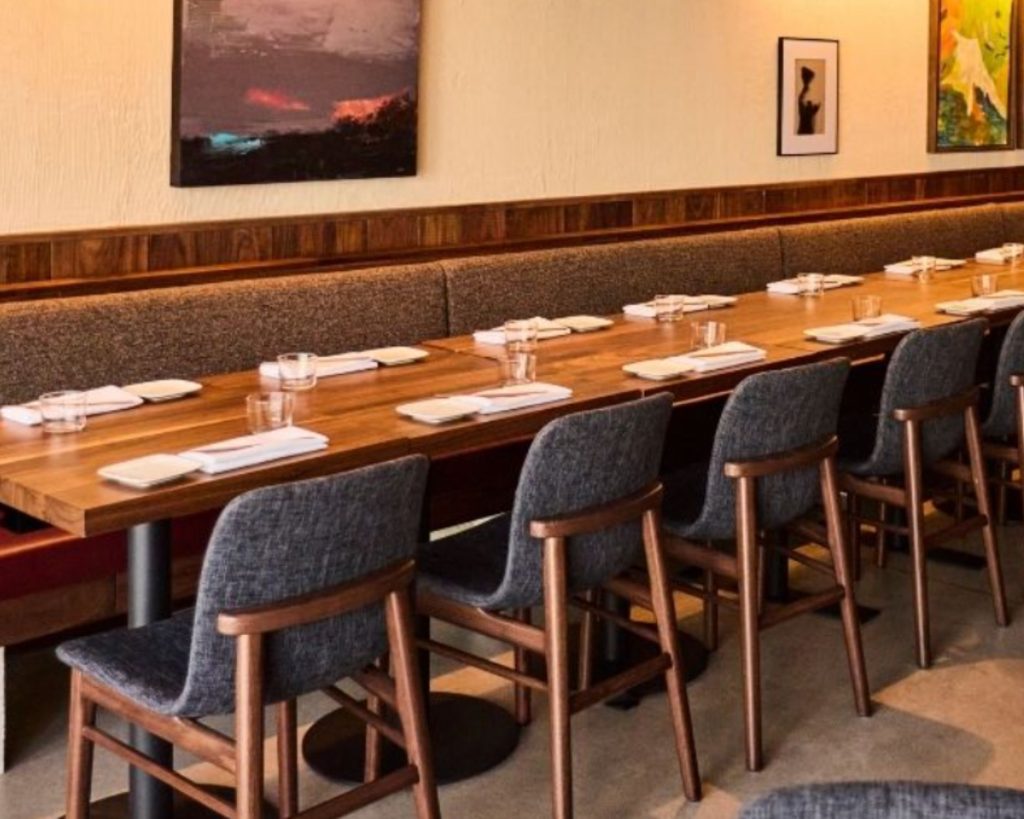 Uchiko Denver interior with long wooden dining table, sleek charcoal grey chairs, and paintings on the wall.